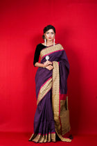 Woman wearing a purple and gold traditional Indian saree with red border.